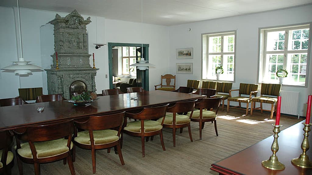 Brandbjerg Manor living room with old furniture. Long table and chairs and an old fireplace.