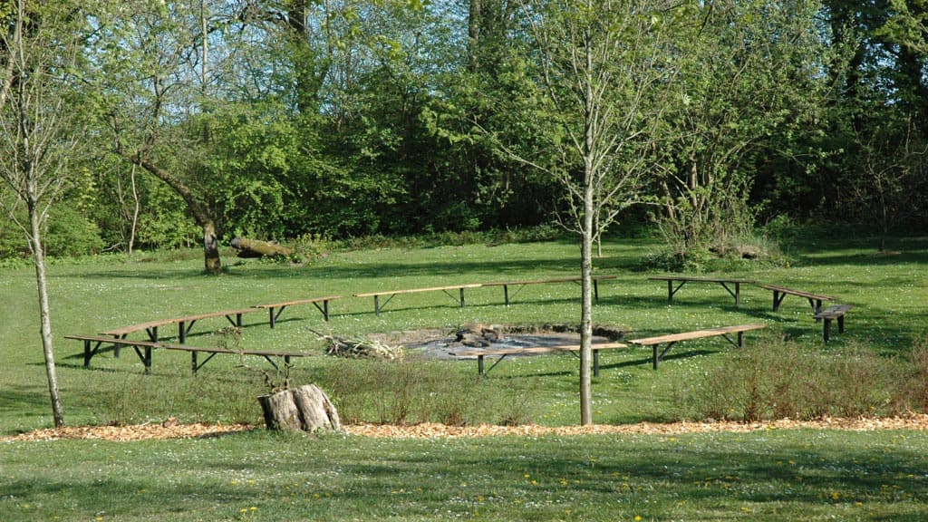 Fire pit with benches in green surroundings and trees around.
